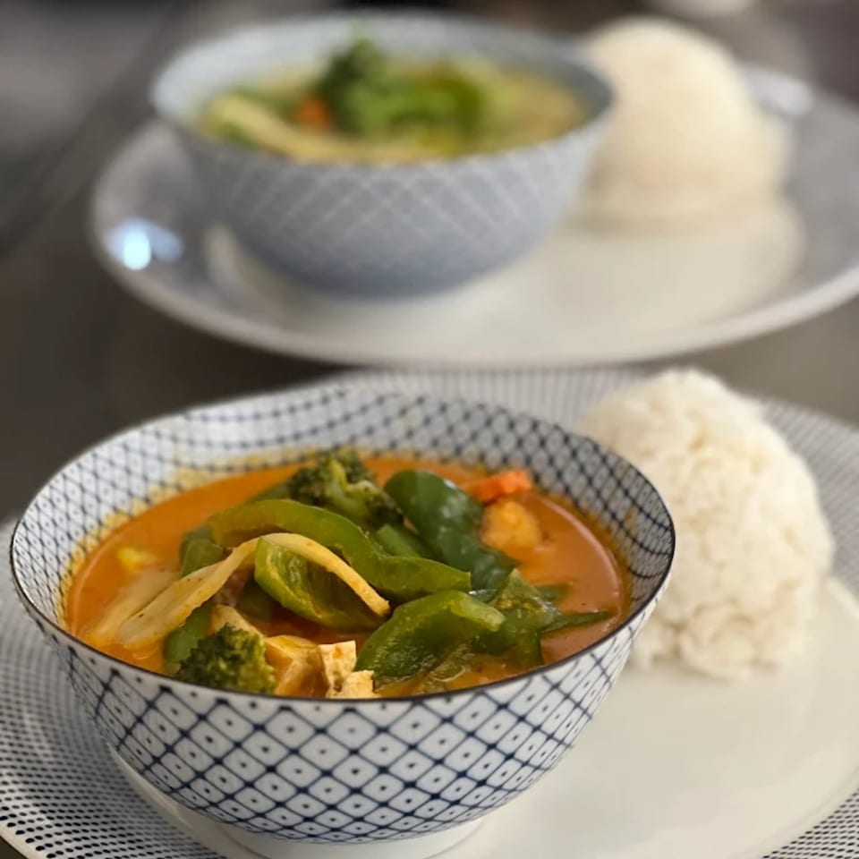 Two bowls of Thai curry, one red and one green, with rice on patterned plates.