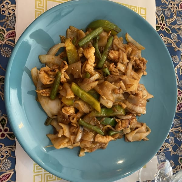 A blue plate of Thai Orchid's Pad See Ew with chicken, wide noodles, onions, and green beans.