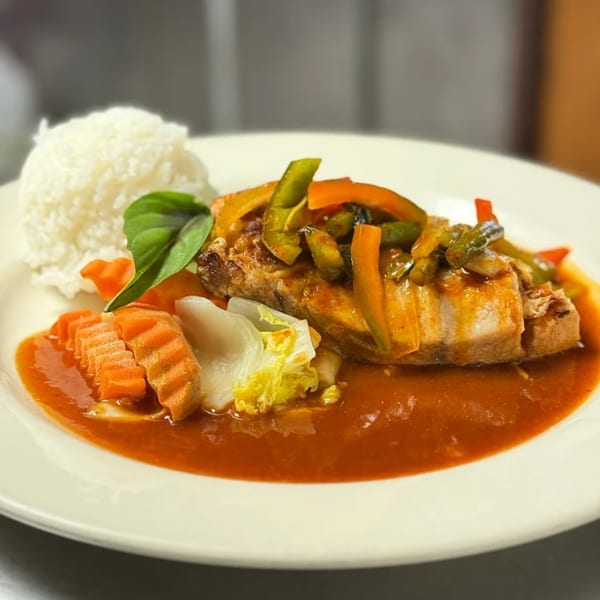 Thai Orchid's red curry with fish, bell peppers, carrots, and rice on a white plate.