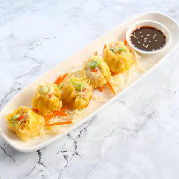 Five Thai Orchid dumplings with shredded carrots, cabbage, and a side of soy sauce.