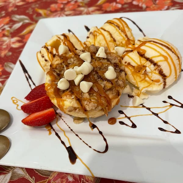 A dessert with a crumble cake, vanilla ice cream, strawberries, and caramel and chocolate drizzle.